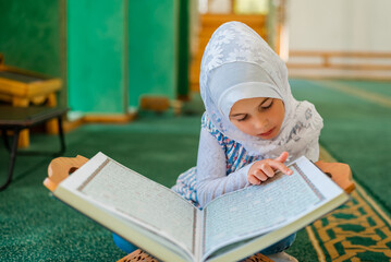 Wall Mural - Muslim child girl learning a holy book Quran in the mosque.