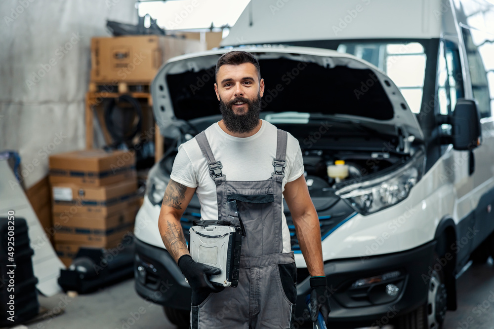 A auto-mechanic with equipment at workshop smiling at the camera.
