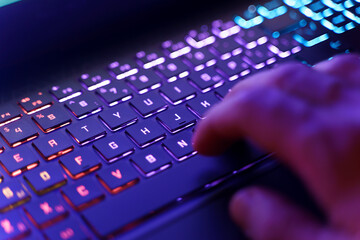 Working on a neon computer keyboard with colored backlighting. Computer video games, hacking, technology, internet concept. Selected focus.