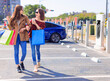 © Tom Wang - Happy  young woman standing on city parking near electric car, charging automobile battery from small city station, holding shopping bags and walking together