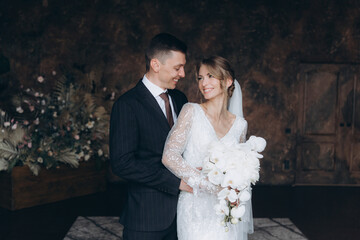 Wall Mural - The first meeting of the groom in a black suit and the bride in a white wedding dress with a bouquet in the interior of a photo studio, hotel, on black background