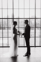 The first meeting of the groom in a black suit and the bride in a white wedding dress with a bouquet in the interior of a photo studio, hotel, on black background