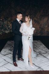 Wall Mural - The first meeting of the groom in a black suit and the bride in a white wedding dress with a bouquet in the interior of a photo studio, hotel, on black background