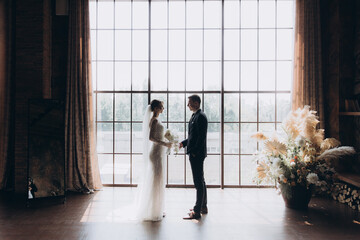 Wall Mural - The first meeting of the groom in a black suit and the bride in a white wedding dress with a bouquet in the interior of a photo studio, hotel, on black background