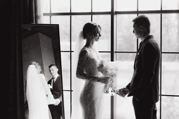 Wall Mural - The first meeting of the groom in a black suit and the bride in a white wedding dress with a bouquet in the interior of a photo studio, hotel, on black background