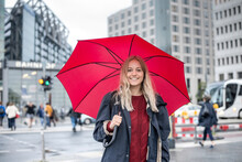 Smiling Young Woman Standing With Red Umbrella On Street