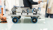 © Westend61 - Model of robotic arm and vehicle on desk with technicians shaking hands standing in background at factory