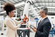 © Westend61 - Smiling developer showing model of robotic arm to businessman in factory