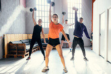 Young Men And Woman With Fitness Instructor Lifting Dumbbells In Gym