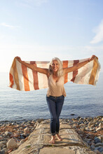 Happy Woman With Arms Outstretched Holding Blanket Enjoying At Beach On Sunny Day