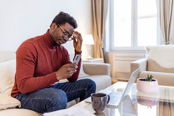 African man sit on couch using smartphone shocked by reading online news, surprised male get breaking message or text on mobile phone, confused guy holding cell see warning notification