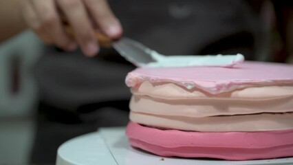 Sticker - A woman spreads cream on top of the cake layers.Decorating pink cake with fresh strawberries pieces.