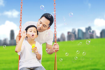 Wall Mural - Child blowing soap bubbles with father at park