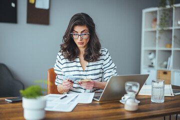 A busy black-haired business woman calculates expenses on a calculator, the number of women estimates household expenses, considers estimating bills and taxes at home