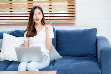 Wall Mural - Beautiful young asian woman working on laptop computer and thinking idea on sofa at home, freelance girl sitting on couch using notebook to internet at living room, one person, lifestyle concept.