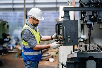 Mechanical engineer or Worker in a safety uniform wearing glasses working with a metal plate drilling machine in the metal lathe factory,