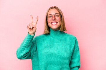 Wall Mural - Young caucasian woman isolated on pink background joyful and carefree showing a peace symbol with fingers.