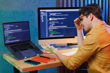 Side view young confused minded puzzled sad software engineer IT specialist programmer man in shirt work at home writing code on laptop pc desktop computer checking virus. Program development concept.