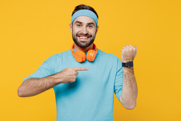 Young fitness trainer instructor sporty man sportsman in headband blue t-shirt spend weekend in home gym using point finger on smart watch isolated on plain yellow background. Workout sport concept.