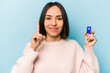 © Asier - Young hispanic woman holding batteries isolated on blue background showing number one with finger.