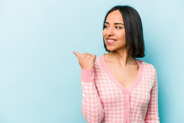 Wall Mural - Young hispanic woman isolated on blue background points with thumb finger away, laughing and carefree.