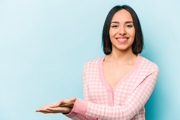 Young hispanic woman isolated on blue background holding a copy space on a palm.