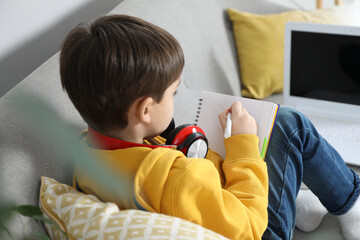 Wall Mural - Cute little boy with headphones and modern laptop studying online at home. E-learning