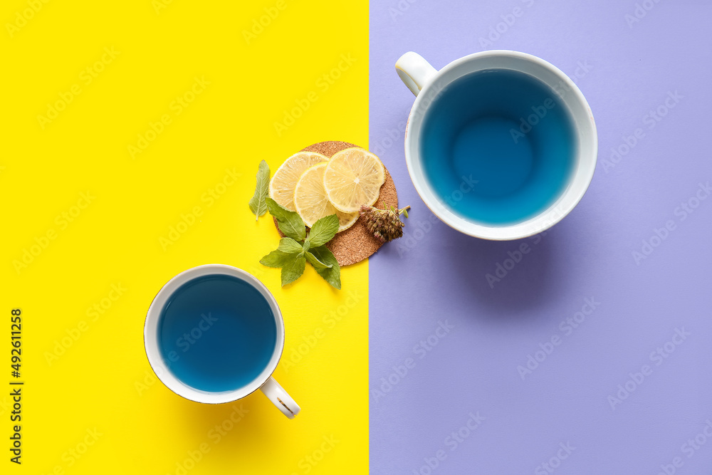 Cups of blue tea and lemon on color background
