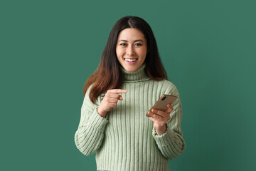 Beautiful young Asian woman with mobile phone on green background