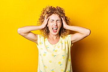 Wall Mural - screaming young girl in shock holding her head with her hands on yellow background.