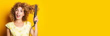 Happy Young Woman With Curly Hair Straightens Her Hair With A Hair Straightener On A Yellow Background. Banner.