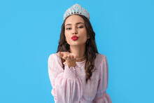 Beautiful Young Woman In Stylish Dress And Tiara Blowing Kiss On Blue Background