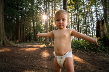 Baby In Diaper Stands With Arms Outstretched In Forest