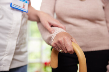 Wall Mural - Close Up Of Senior Woman With Hands On Walking Stick Being Helped By Care Worker