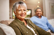 © Tasneem H/peopleimages.com - We did good. Portrait of a happy older woman relaxing on the sofa with her husband in the background.