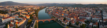 Panoramic Aerial View Of Maribor, Slovenia Early In The Morning. Red Bridge Crossing River In A Peaceful Town In Europe. Many Houses With Red Roofs From Drone View.