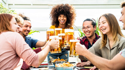 Wall Mural - Mixed race group of friends toasting beer glasses at brewery pub - Happy young people having indoor dinner party celebrating summertime together - Beverage, food and friendship lifestyle concept