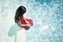 Abstract Portrait Of G With Black Hair In Red Dress Sitting On Edge Of Swimming Pool In Summer