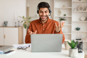 Arab man using laptop wearing headset sitting at desk