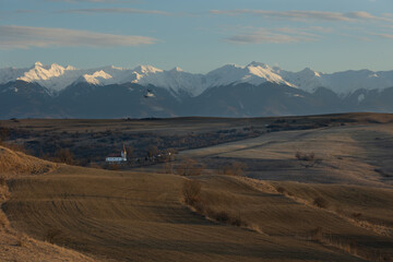 Medieval church in a valley at sunset. The Făgărași Mountains in the background in Fofeldea, Sibiu, Romania. Plow land.