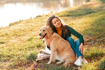 Wall Mural - Smiling woman hugging her pet golden retriever dog near face. Golden retriever dog playing with a curly woman walking outdoors sunny day. love and care for the pet.