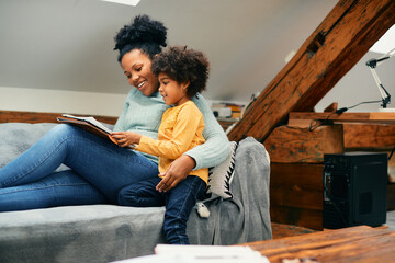 Wall Mural - Happy black mother relaxing on sofa while daughter is showing her what she drew on paper.