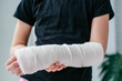 Close-up of a broken arm of a child in a cast. The girl holds her hand bent on the background of a black t-shirt.