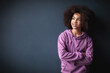 Portrait of positive dark skinned smile female teenager crossed arms, wears lilac hoodie over blue studio