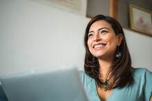Close Up Of Smiling Latin Woman Looking Aside With Laptop At Home