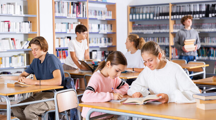 Two female friends reading books together and preparing for exams in the school library