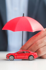 Sticker - Businessman hand holding umbrella and cover  red car toy on table. Car insurance, warranty, repair, Financial, banking and money concept