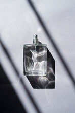 Transparent Bottle Of Perfume With Spray On A Grey Background. Beautiful Natural Light And Shadows. Mockup Of Clear Glass Fragrance Without Lid . Cosmetics Packaging Container Top View.