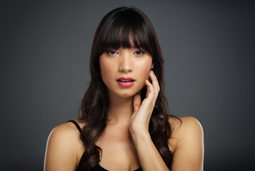 Perfect face, perfect skin. Studio shot of a beautiful young woman posing with her hand on her face against a dark background.