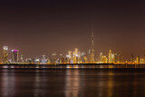 Fototapeta  - Dubai Business Bay skyline at night with colorful illuminated buildings and calm Dubai Creek water.